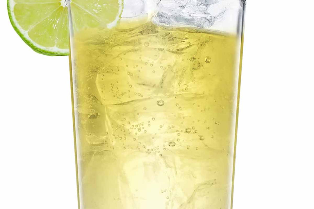 A tall glass filled with a sparkling yellow drink, garnished with a lime wedge on the rim, and containing ice cubes.